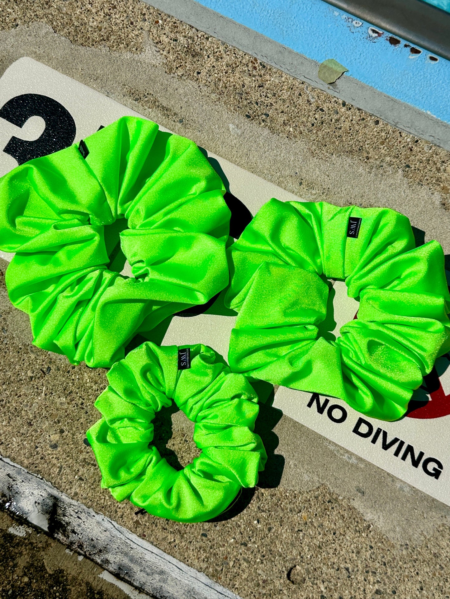 Three bright green scrunchies on a no diving sign by a pool.